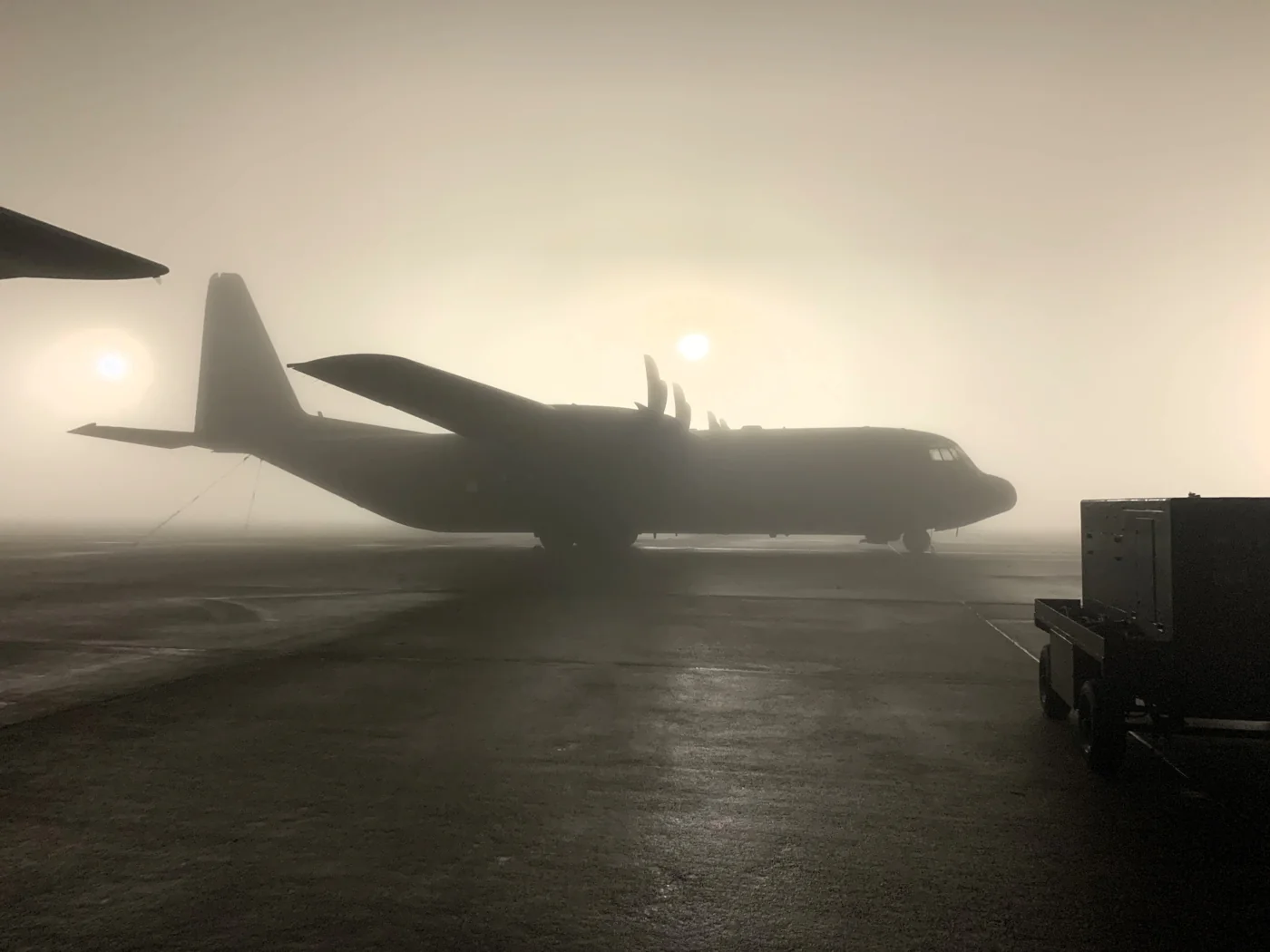 A transport aircraft silhouetted in fog on an airfield